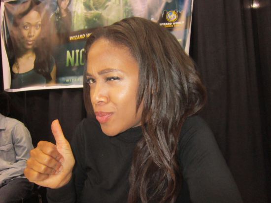 Nicole Beharie at a convention table, winking and giving a thumbs-up.