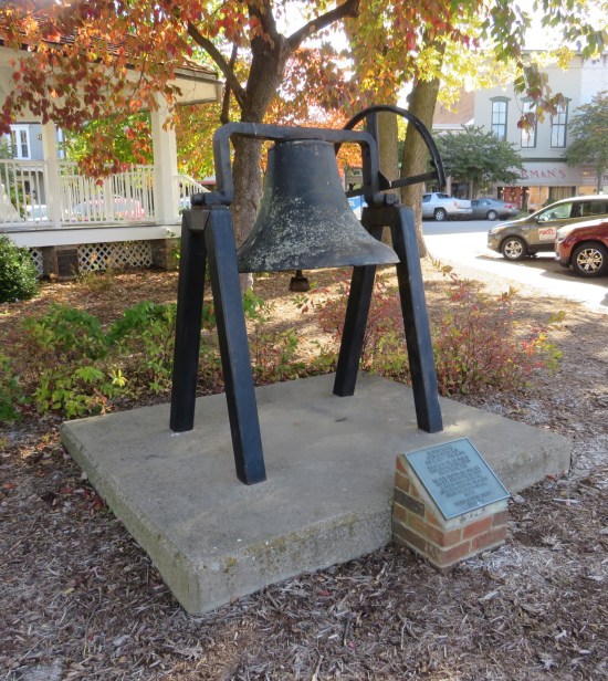 An early 1800s church bell hung at ground level in the grassy town square.