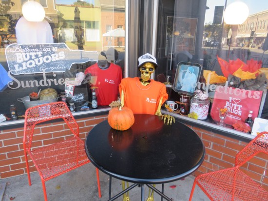 A Halloween skeleton sitting at a table outside Butt Drugs.