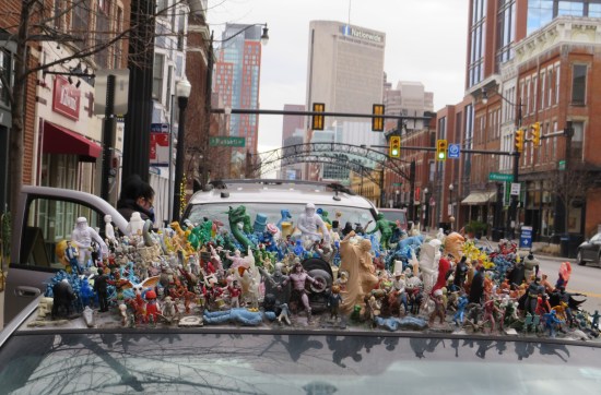 A bunch of toys glued to a car roof; downtown Columbus is hazy in the distant background.