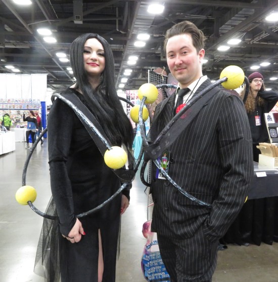 Cosplay: Morticia and Gomez Addams, but surrounded by atomic electron orbits.
