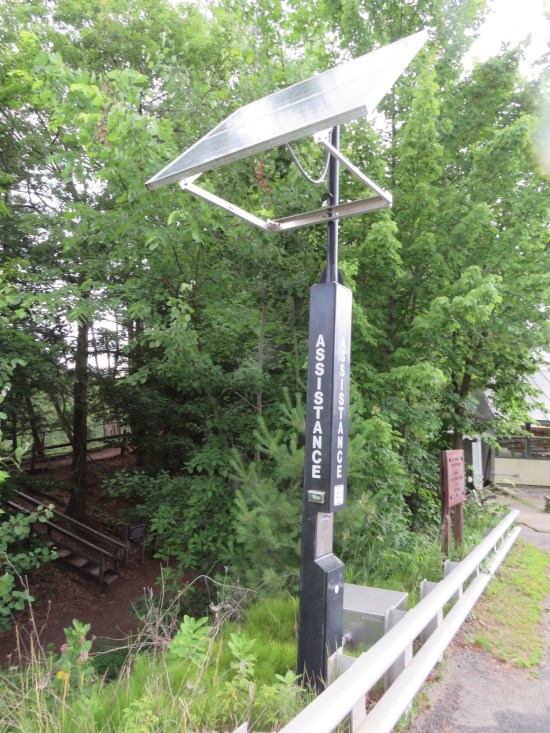 A thin black "assistance" hotline stand with solar panels on top.