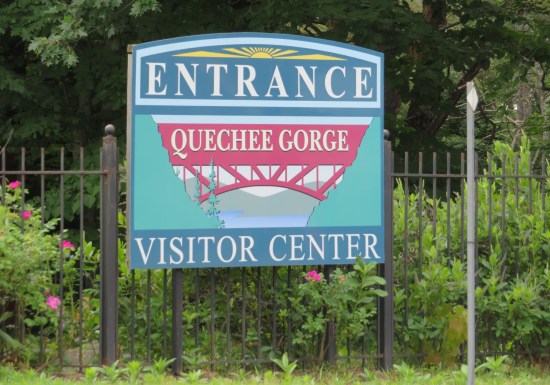 Quechee Gorge State Park Visitor Center sign, blue with white lettering and a red silhouette of a bridge in the center.