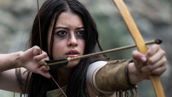 Amber Midthunder as an 18th-century Native preparing to attack with bow and arrow.