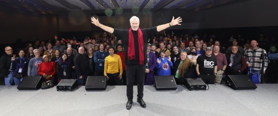 John de Lancie on a stage accompanied by hundreds of Star Trek fans.