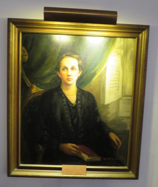 Painting: woman in a black dress sitting near an open shutter, closed book in her lap.