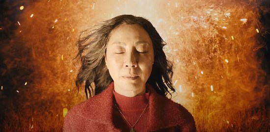 Michelle Yeoh looking peaceful, eyes closed, with an explosion behind her.
