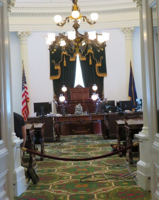 A roped-off view of a state congressional chamber, green carpet.
