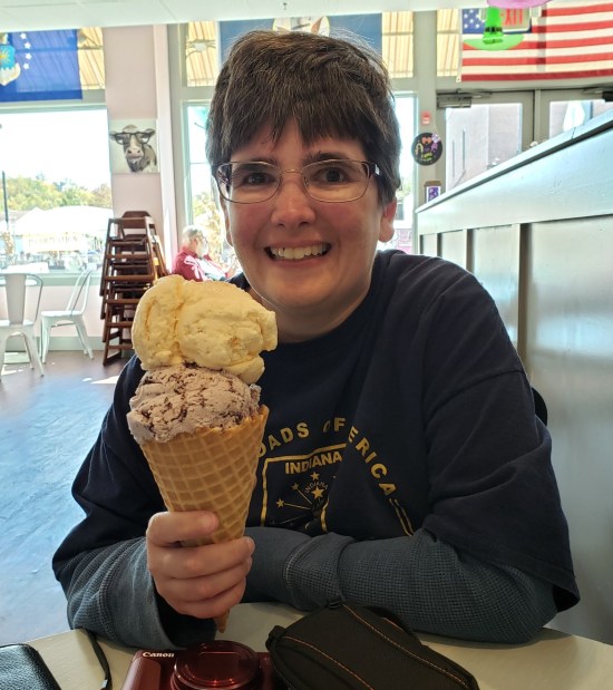 Anne smiling bigly and holding a large ice cream cone with two massive scoops that nearly add up to the size of her head.