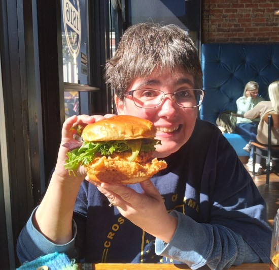Anne smiling while holding up a Pork Tenderloin sandwich with both hands.