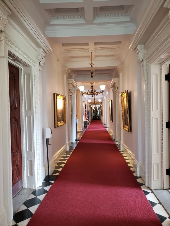 A long, deserted, red-carpeted hallway through the State House.