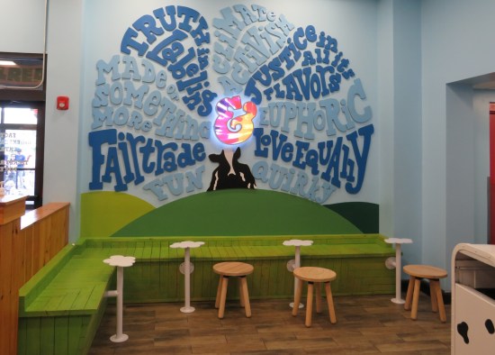 A mission statement list of cheerfully Earth-friendly objectives in '60s psychedelic font, on a wall above a green bench.