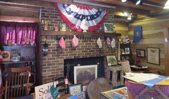 A brick fireplace surrounded with a LOT of stuff of varying historical and geographical value, all hanging from or leaning against or piled next to it.