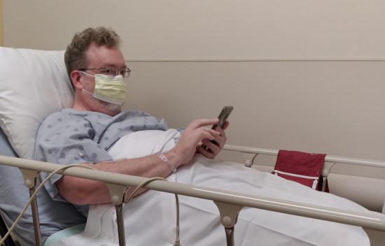 Me in a hospital bed with a mask and IV, playing on my phone.