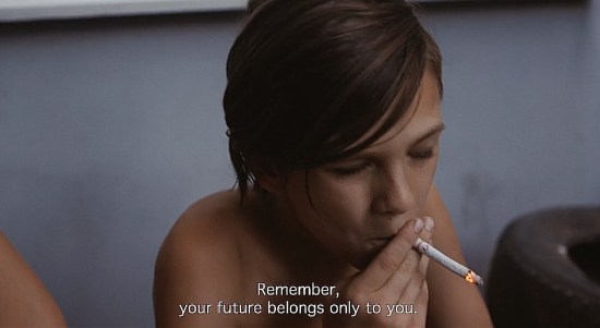A young teen boy sitting outside, smoking a cigarette while an offscreen adult tells him, "Remember, your future belongs only to you."