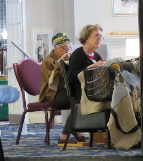Two members of a sewing circle, sewing while watching a TV offscreen.