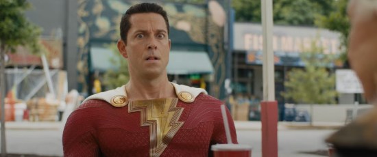 Zachary Levi as Shazam, sitting at a park table and looking scared and confused while Helen Mirren (offscreen) says menacing things.
