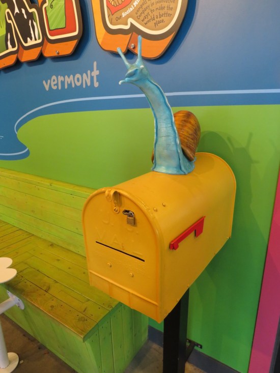 A cartoonish yellow mailbox with a six-inch-tall snail statue on top.