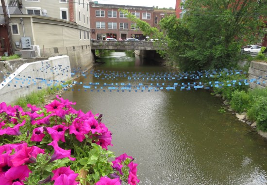 A river flows through the city with blue decorations strung across, and purple flowers in the foreground.