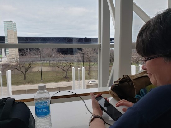 Anne at the table, charging her phone and looking out the window at Chicago's shoreline on Lake Michigan.