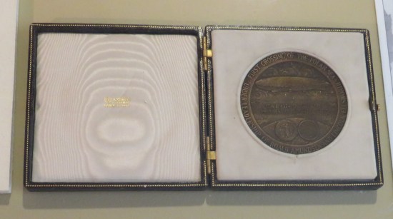 Bronze medal stored in a booklet. On the medal, a picture of a blimp ringed by the words "First Crossing of the Polar Sea Under Leadership of Roald Amundsen and Lincoln Ellsworth".