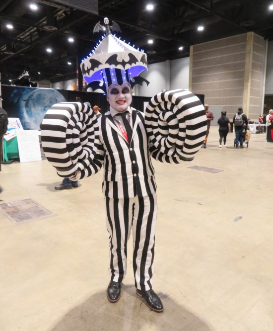 cosplay: Beetlejuice with both arms extra-long and curling up, reenacting a scene from his film.
