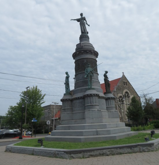 A three-tier obelisk with a robed woman on top, two soldiers flanking her on the middle level, and steps all around the base. It's in the middle of a roundabout.
