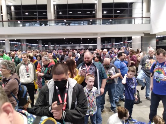 Large crowd waiting to enter a comic con. A few fans wear non-cosplay masks.
