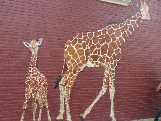 A red brick wall with two giraffes painted on it, one adult and one kid.