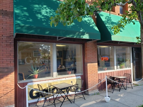 Diner with "GOLDEN'S" stenciled on the window and a neon OPEN sign. Two empty patio tables are outside behind a white chain.