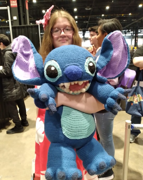 Lilo cosplayer holding a stuffed Stitch nearly as big as her.