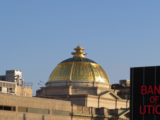 A shiny gold dome amid several tall buildings on a cloudless day.