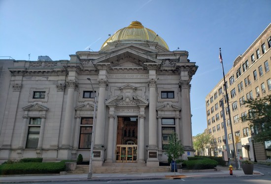 An old-fashioned bank with Greco-Roman columns, ornate wooden door and that same gold dome on top.