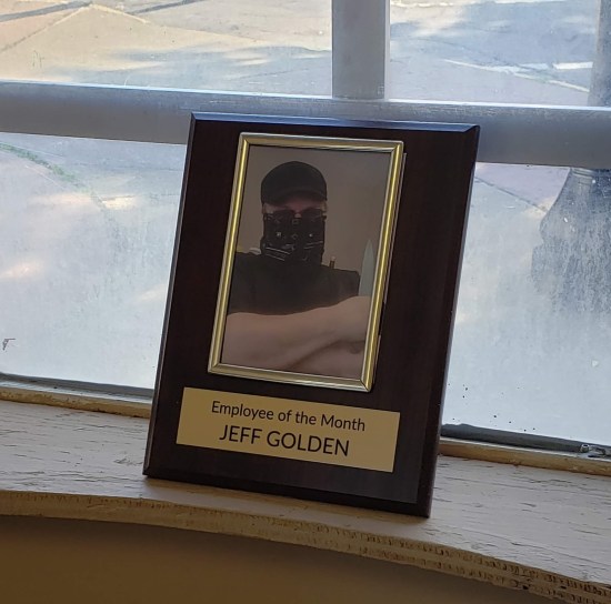 A framed photo of the owner himself wearing a pandemic mask and blue baseball cap, holding a large knife. The frame labels him "Employee of the Month".