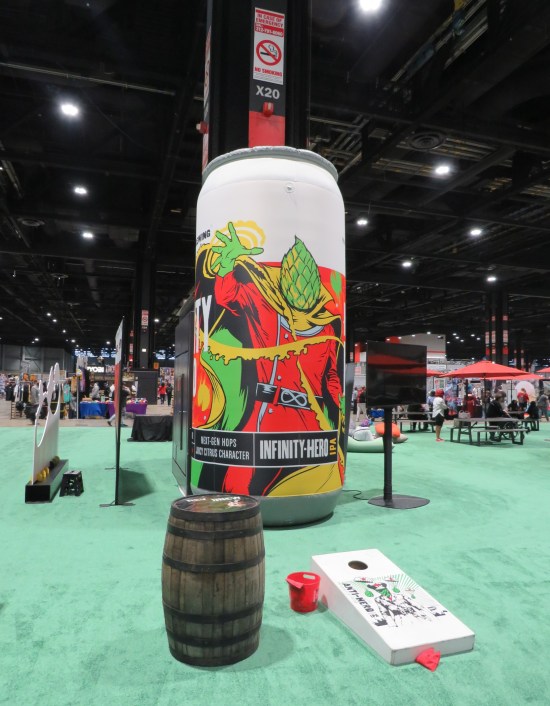 A big inflatable beer can with a superhero on it, in the middle of an area covered in key lime green carpet.