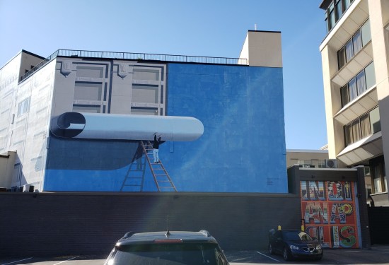 A mural of a guy putting up wallpaper over a building.