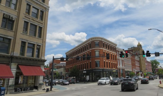 A downtown corner with mostly brown brick buildings, including a bookshop. Lunchtime traffic is a bit heavy around us.