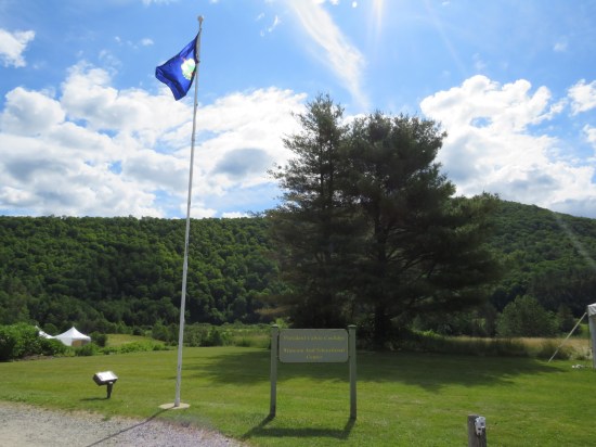 The Coolidge State Historic Site sign and flag by the parking lot, with the Green Mountains looming in the sunny horizon.