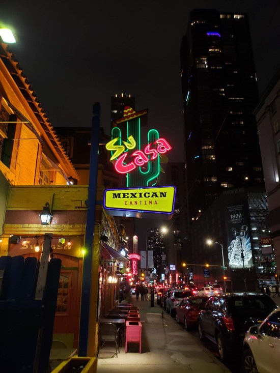 Su Casa's neon sign at night, with other big-city lights dotting the background.