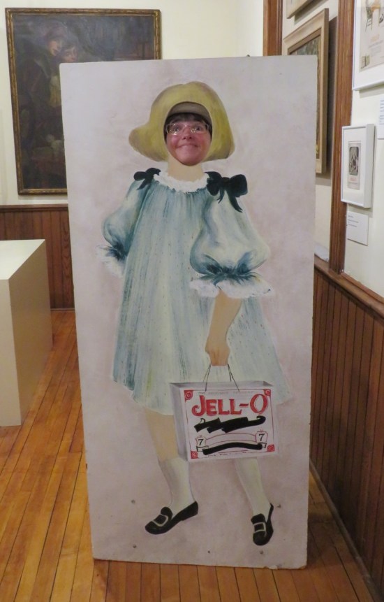Anne sticking her face through a cardboard standee of a 1920s Jell-O girl.