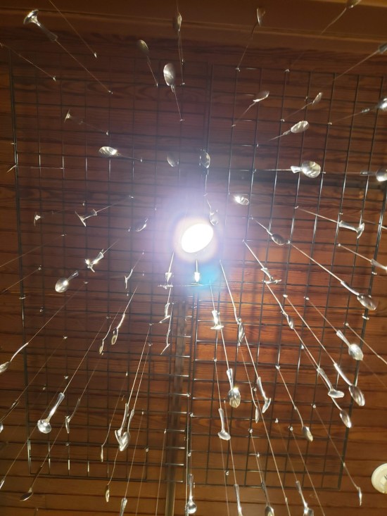 Dozens of metal eating utensils hanging from the ceiling and pointing directly at you looking up.