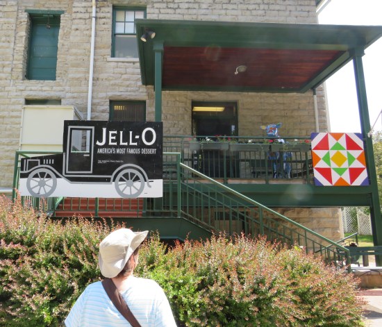 Anne looking up at the two-story Jell-O Museum. Second floor has a balcony with a cow statue on it.