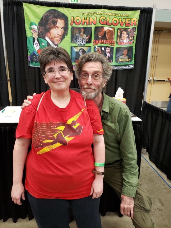 John Glover crouching down next to Anne in front of his booth.