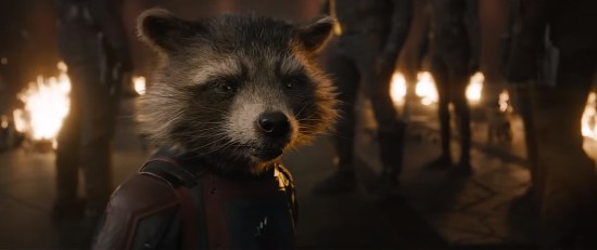 Rocket mid-speech, surrounded by his friends' legs.