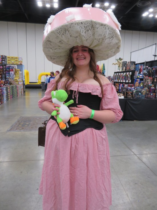 costume: Toadette with a very wide-brimmed mushroom hat and holding a stuffed Yoshi doll.