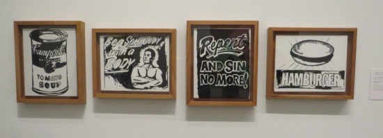 Four small, black-and-white paintings by Andy Warhol hanging in a line on an otherwise blank wall. Refer to caption.