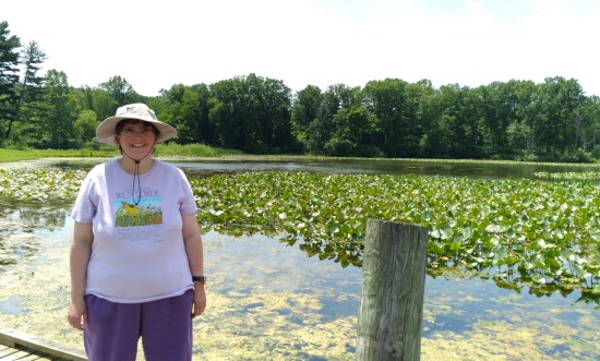 Anne smiling and standing next to the lily-pad-covered side of the lake.