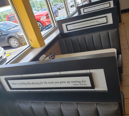 Diner booths with inspirational quotes on placards atop each one. In front is from Milton Bradley: "There is nothing like playing for the team you grew up rooting for," Next booth back is from songwriter Samuel F. Smith: "From every mountain side [sic], let freedom ring."