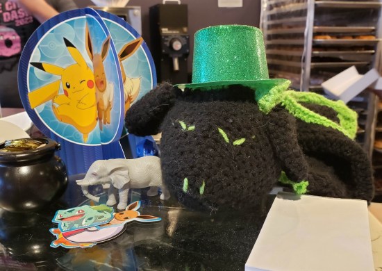 Atop the vitrine, a felt dragon wearing a St. Patrick's hat and a cardboard Pikachu party decoration.