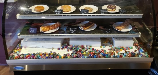 A vitrine with some donuts in it. The bottom shelf holds dozens and dozens of dice in different sizes.